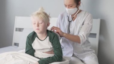 Doktor, öksüren bir çocuğun steteskobunu dinliyor. 
