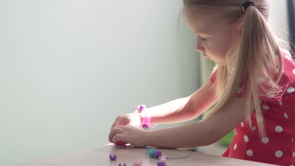 Egy csinos lány karkötőt készít a varráshoz használt gyerekekből. — Stock videók