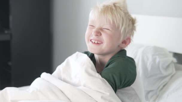 Beautiful blond boy laughs in the morning in bed — Stock Video