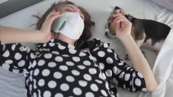 Eine Frau in Quarantäne liegt mit einem niedlichen Welpenbeagle im Bett — Stockvideo