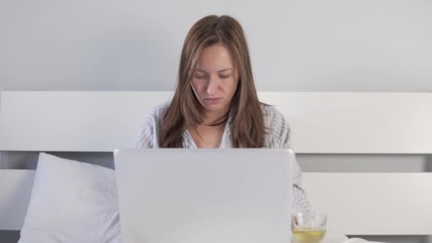 A woman with a cold works at the computer and drinks tea with lemon — Stock Video