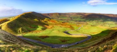 Long and winding rural road of Winnat Pass leading through green hills in Peak District, United Kingdom. clipart