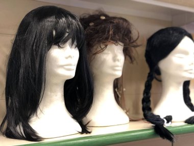 Mağazada siyah ve koyu kahverengi peruklu kadın mankenler var. Saç kesimi. Kuaför.