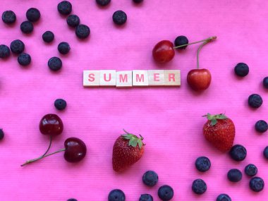 Summer - word spelled with letter pieces on pink background covered with cherries, blueberries, strawberries. Summer background