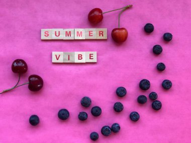 Summer vibe - written with letter pieces on pink background with cherries and blueberries. Summer concept. Top view. Mock-up