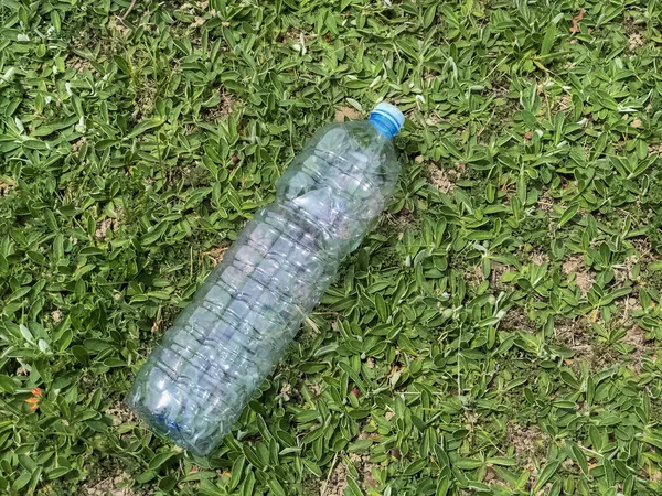 Empty plastic bottle on green grass close-up top view. Copy space. Plastic garbage, recycle. Ecological concept