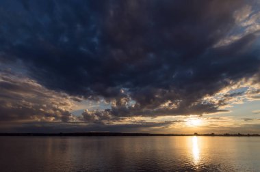 Big cloud over the Tom river in the light of sunlight.Sunset on the waterfront Tom. The dark blue-and-gray cloud closed half the sky. Bright Sun on the horizon.