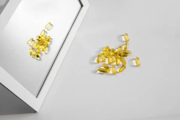 yellow medical vitamin capsules lies on a white table and is reflected in the mirror