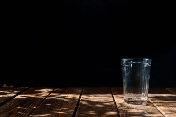 Vidro transparente vazio em um fundo escuro. mesa de madeira marrom horizontal. sol brilhante — Fotografia de Stock