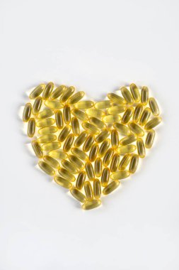 Beyaz arka plan vitaminlerinde bir avuç sarı kalp şeklindeki haplar sağlıklı yağ balığı yağına iyi gelir.