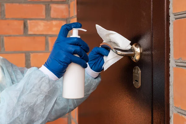 Γυναίκα που καθαρίζει ένα χερούλι πόρτας με σπρέι απολύμανσης και μαντηλάκι μίας χρήσης — Φωτογραφία Αρχείου