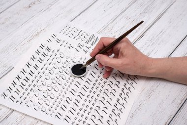 Kaligrafi kağıtları, kalem uçları, kağıt, tahta arka planda mürekkep. Boya fırçasıyla yazılmış İngiliz alfabesinin harfleri.