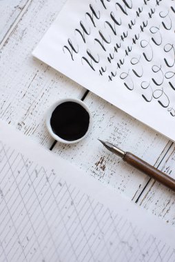 Kaligrafi kağıtları, kalem uçları, kağıt, tahta arka planda mürekkep. Boya fırçasıyla yazılmış İngiliz alfabesinin harfleri.