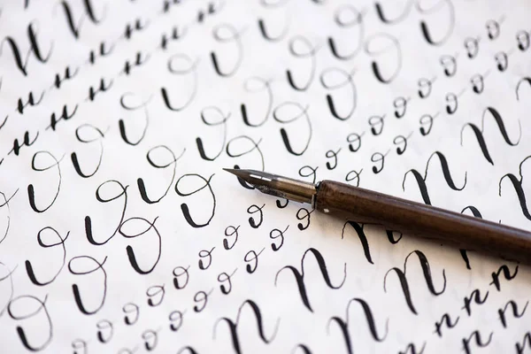 Hojas de caligrafía, plumas, papel, tinta sobre un fondo de madera. Cartas del alfabeto inglés escritas con un pincel . —  Fotos de Stock