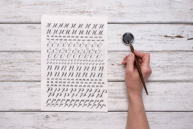 Kaligrafi kağıtları, kalem uçları, kağıt, tahta arka planda mürekkep. Boya fırçasıyla yazılmış İngiliz alfabesinin harfleri.