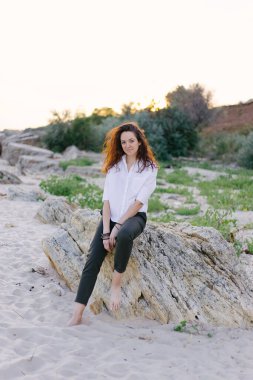 Kumsalda oturan bir kadın. Çiller, koyu renk saçlar