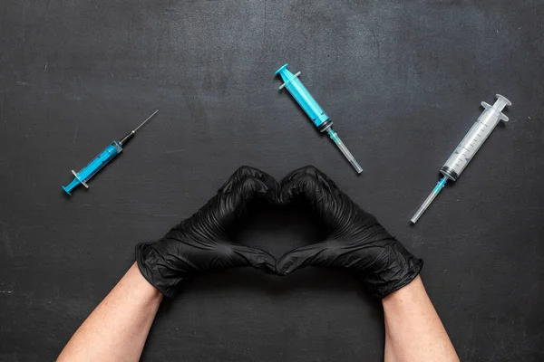 黒の黒板の背景に異なるサイズの医療注射器。心臓の形をした医療用手袋の手 — ストック写真