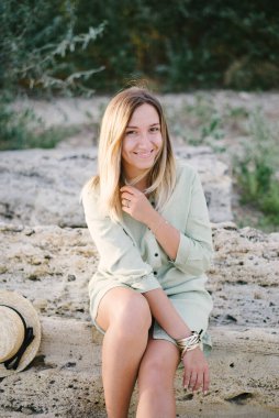 Vahşi bir plajda oturan, taşlı bir kadın. Sarışın.