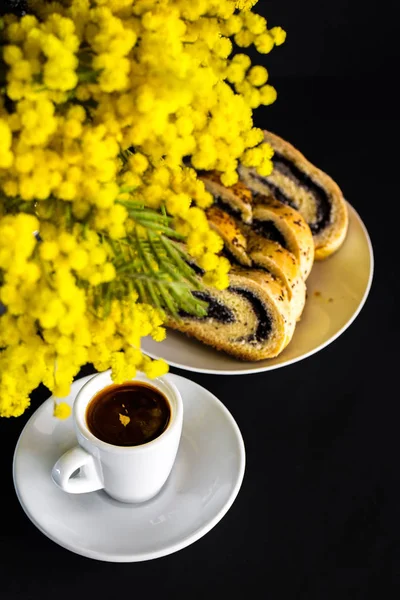 Mimoza dalları, fincan kahve ve haşhaş tohumu strudel siyah bir zemin üzerine