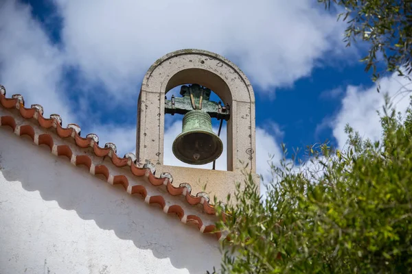 Kilise bell beyaz bulutlar ve zeytin ağaçlarının yeşil bitki örtüsü ile mavi gökyüzü karşı çatıda