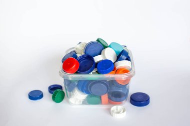 Beyaz arka plandaki bir konteynırda çeşitli şişeler için bir sürü renkli plastik kapak. Plastik atıkları geri dönüştürüyorum. Çöpleri ayırmak. Dünyayı geri dönüşümlü kampanyadan kurtar