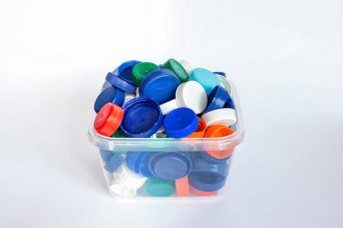 Beyaz arka plandaki bir konteynırda çeşitli şişeler için bir sürü renkli plastik kapak. Plastik atıkları geri dönüştürüyorum. Çöpleri ayırmak. Dünyayı geri dönüşümlü kampanyadan kurtar