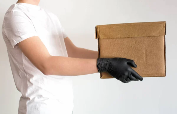Person in white t-shirt and black gloves giving donation cardboard box, isolated on white background, copy space. Coronavirus volunteer charity donations. Making donations to food bank