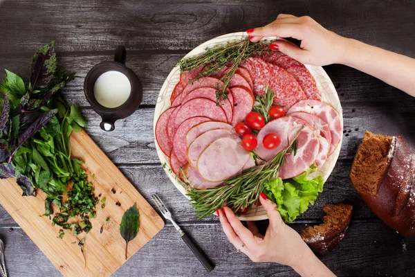 Gesneden worst, handen met de schotel, houten aanrecht, gehakte basilicum — Stockfoto