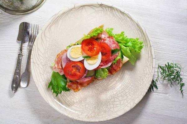 Casa sanduíche sub, bacon, salsicha, ovo e verduras em uma baguete, prato, vista superior, ainda vida — Fotografia de Stock