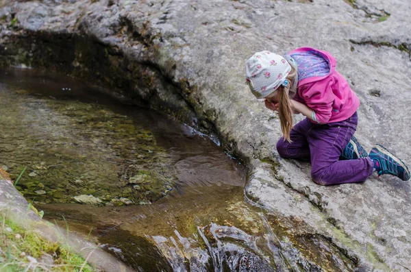 Meisje drinkt uit een bergbeek in het vroege voorjaar — Stockfoto