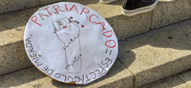 Kartel de cartn hekho a mano para el da da la mujer trabajadora en unas escaleras junto a tres personas. Kartel en espaol haciendo alusin a las reivindicaciones feministleri. 8 De Marzo. Da de la Mujer.