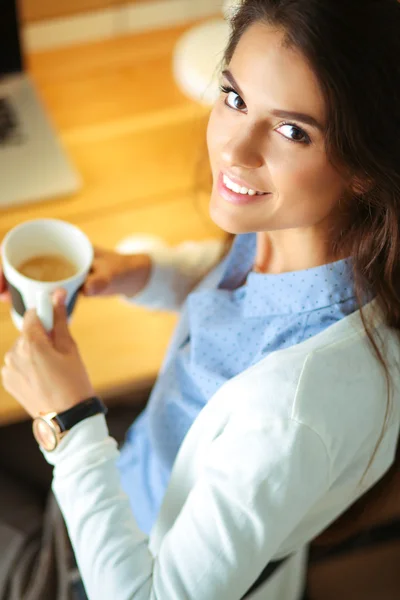 Porträtt av avslappnad ung kvinna sitter vid skrivbordet håller kopp kaffe — Stockfoto