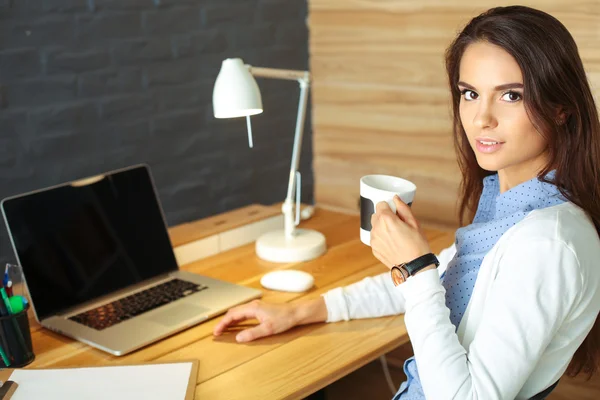 Portrait de jeune femme détendue assise à son bureau tenant une tasse de café — Photo