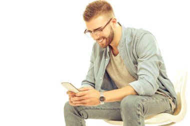 Sandalyede oturan ve cep telefonuyla genç adam