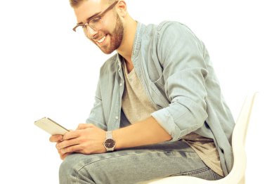 Sandalyede oturan ve cep telefonuyla genç adam