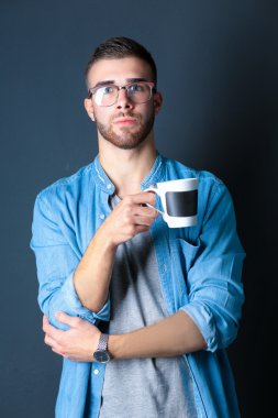 Yakışıklı bir genç adam ayakta ve bir fincan kahve onun elinde tutan portresi