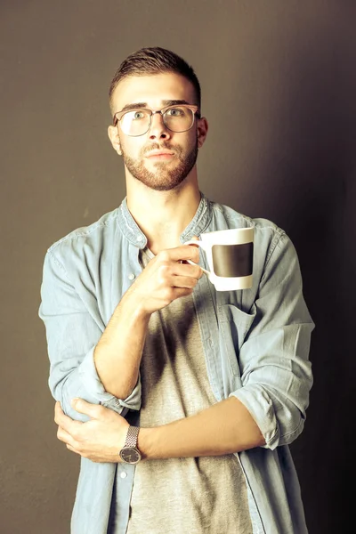 立って、彼の手でコーヒー カップを保持しているハンサムな若い男の肖像 — ストック写真