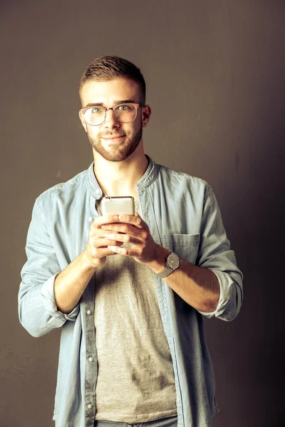 Sorrindo jovem segurando telefone enquanto mensagens de texto — Fotografia de Stock