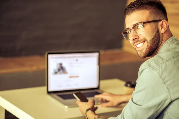 Jonge man met telefoon en werkt op de laptop — Stockfoto