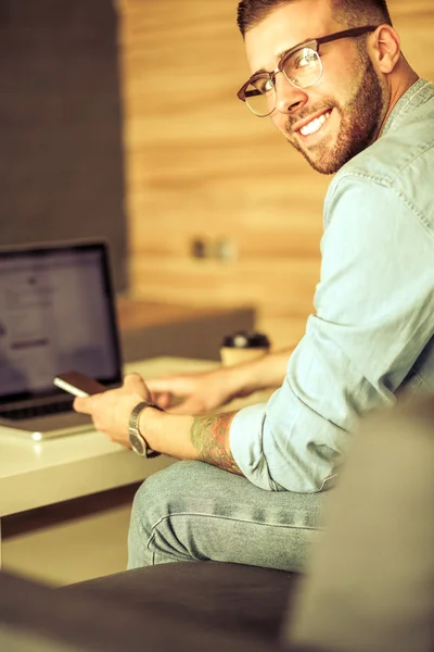 Genç adam kullanarak telefon ve dizüstü bilgisayarda çalışır — Stok fotoğraf