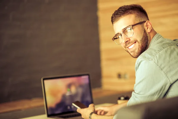 Jonge man met telefoon en werkt op de laptop — Stockfoto