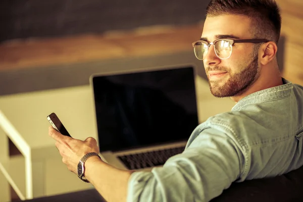 Jonge man met telefoon en werkt op de laptop — Stockfoto