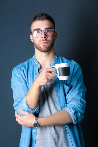 Retrato de un joven guapo de pie y sosteniendo una taza de café en sus manos —  Fotos de Stock