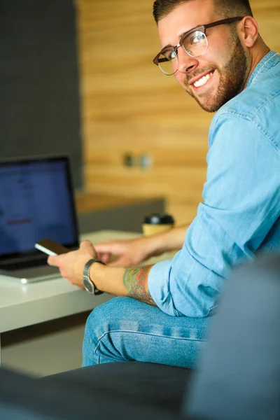 Mladý muž pomocí telefonu a funguje na notebooku — Stock fotografie