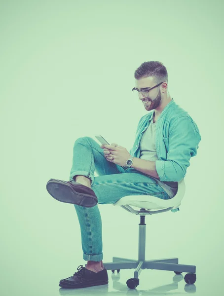 Mladý muž sedí na židli a pomocí mobilního telefonu — Stock fotografie