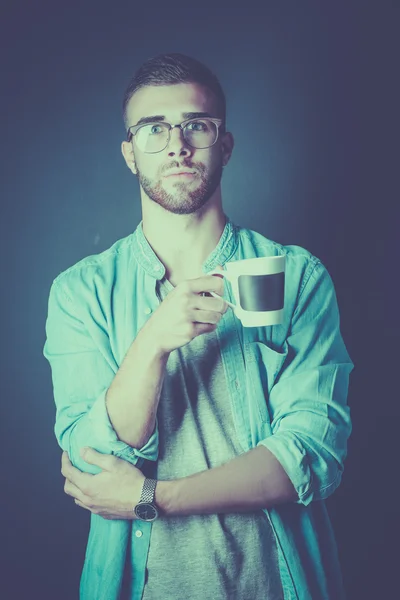 Retrato de un joven guapo de pie y sosteniendo una taza de café en sus manos —  Fotos de Stock