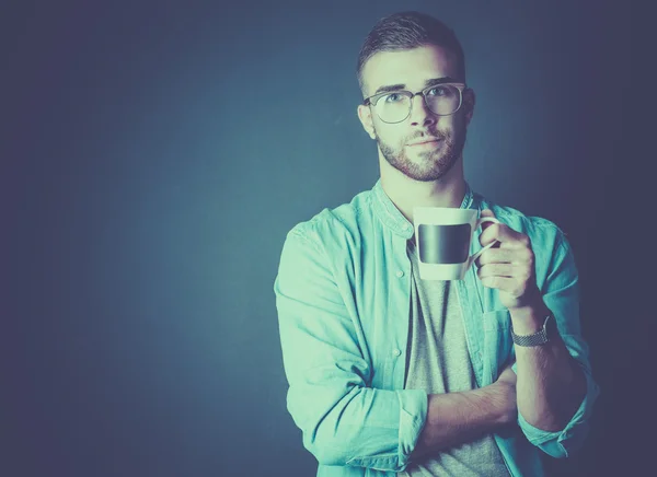 Retrato de un joven guapo de pie y sosteniendo una taza de café en sus manos — Foto de Stock