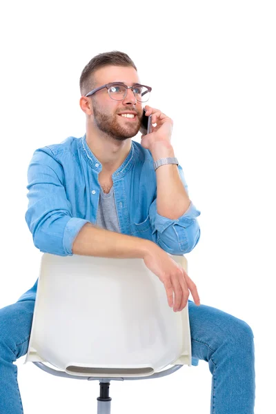 Mladý muž sedí na židli a pomocí mobilního telefonu — Stock fotografie