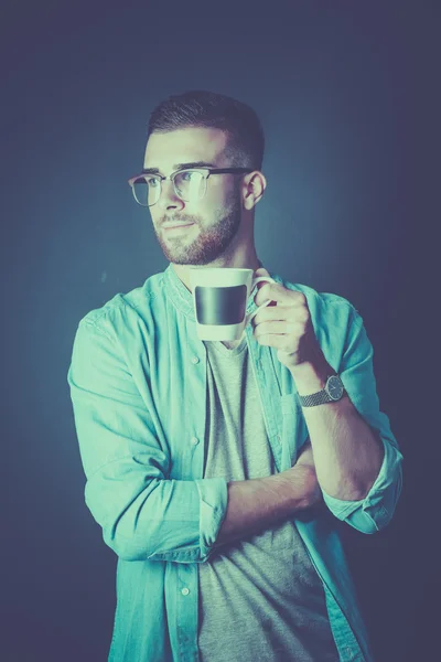 Portret van een knappe jongeman permanent en houden van een kopje koffie in zijn handen — Stockfoto
