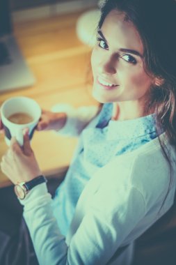 Masasında oturan ve elinde bir fincan kahveyle rahatlamış genç kadının portresi.